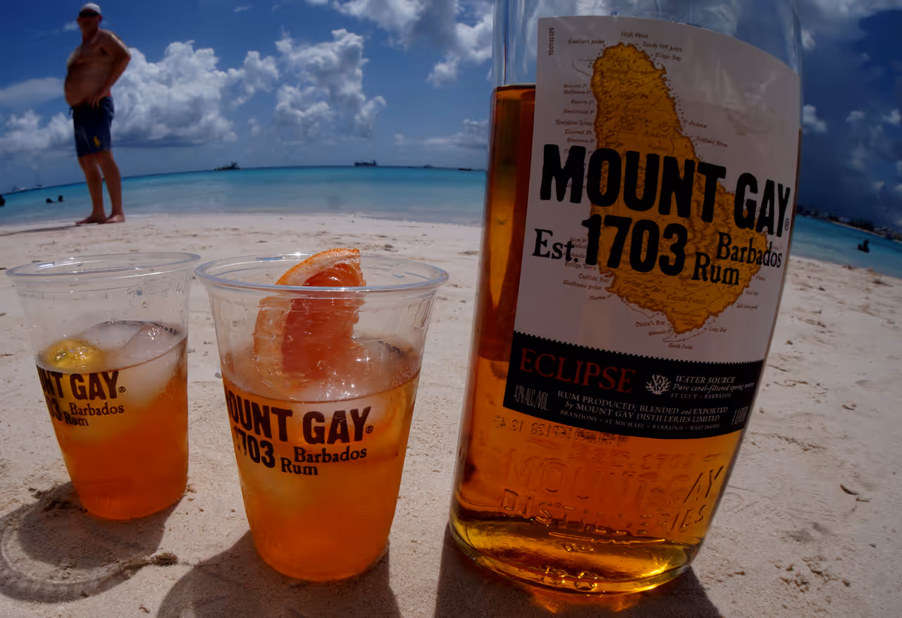 A bottle of Mount Gay Eclipse with two cocktails on a beach in Barbados.