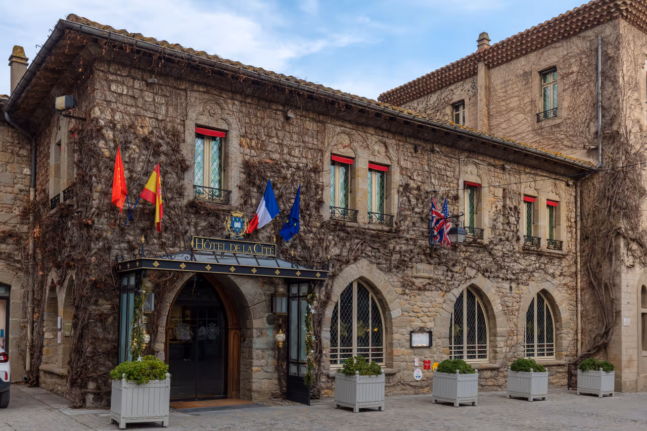 Ivy covered stone facade of the Hotel de la Cite in Carcassonne with international flags over the entrance canopy