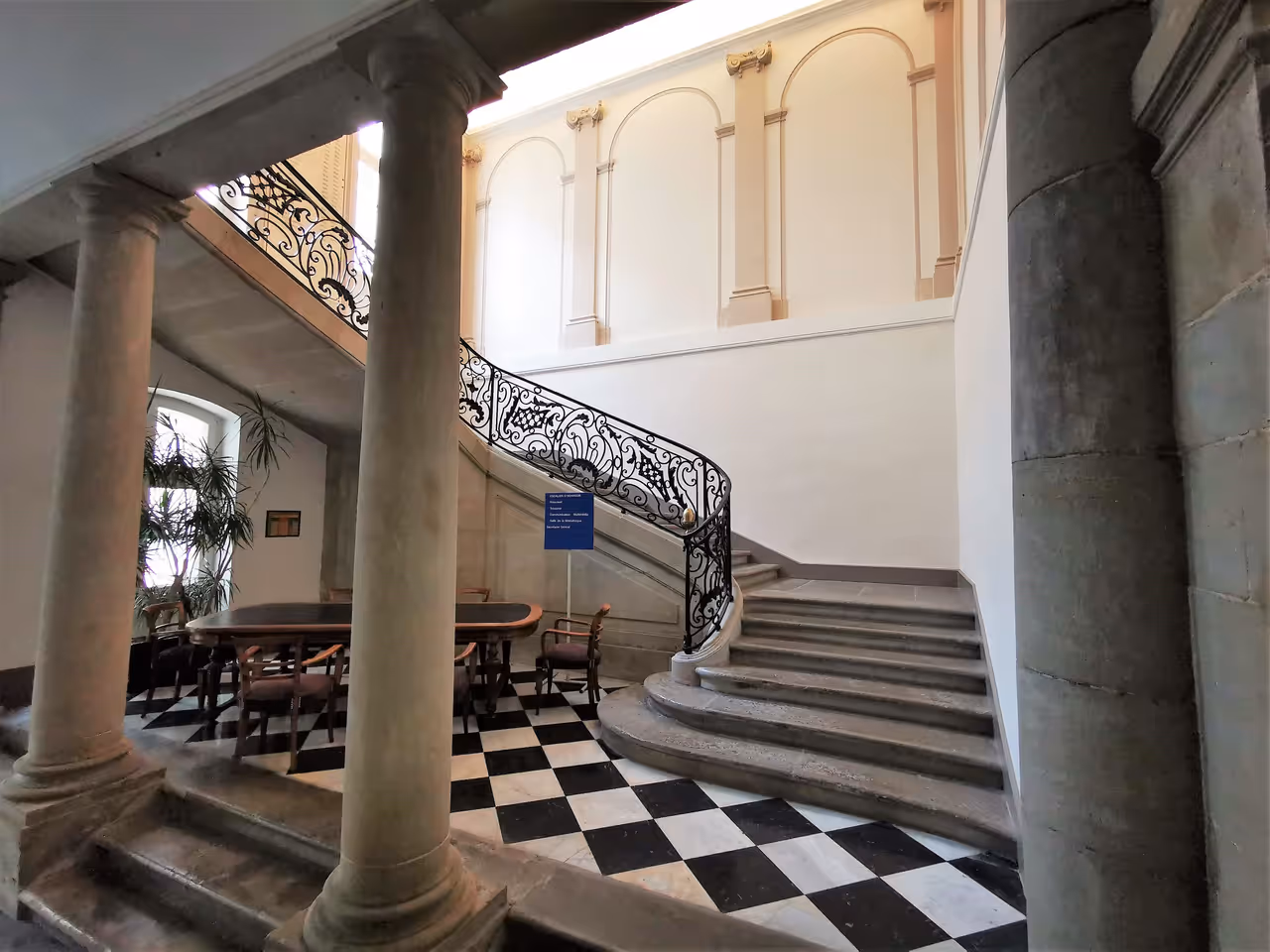 Grand staircase inside the historical Hotel de Murat in Carcassonne with checkered flooring and elegant stone pillars