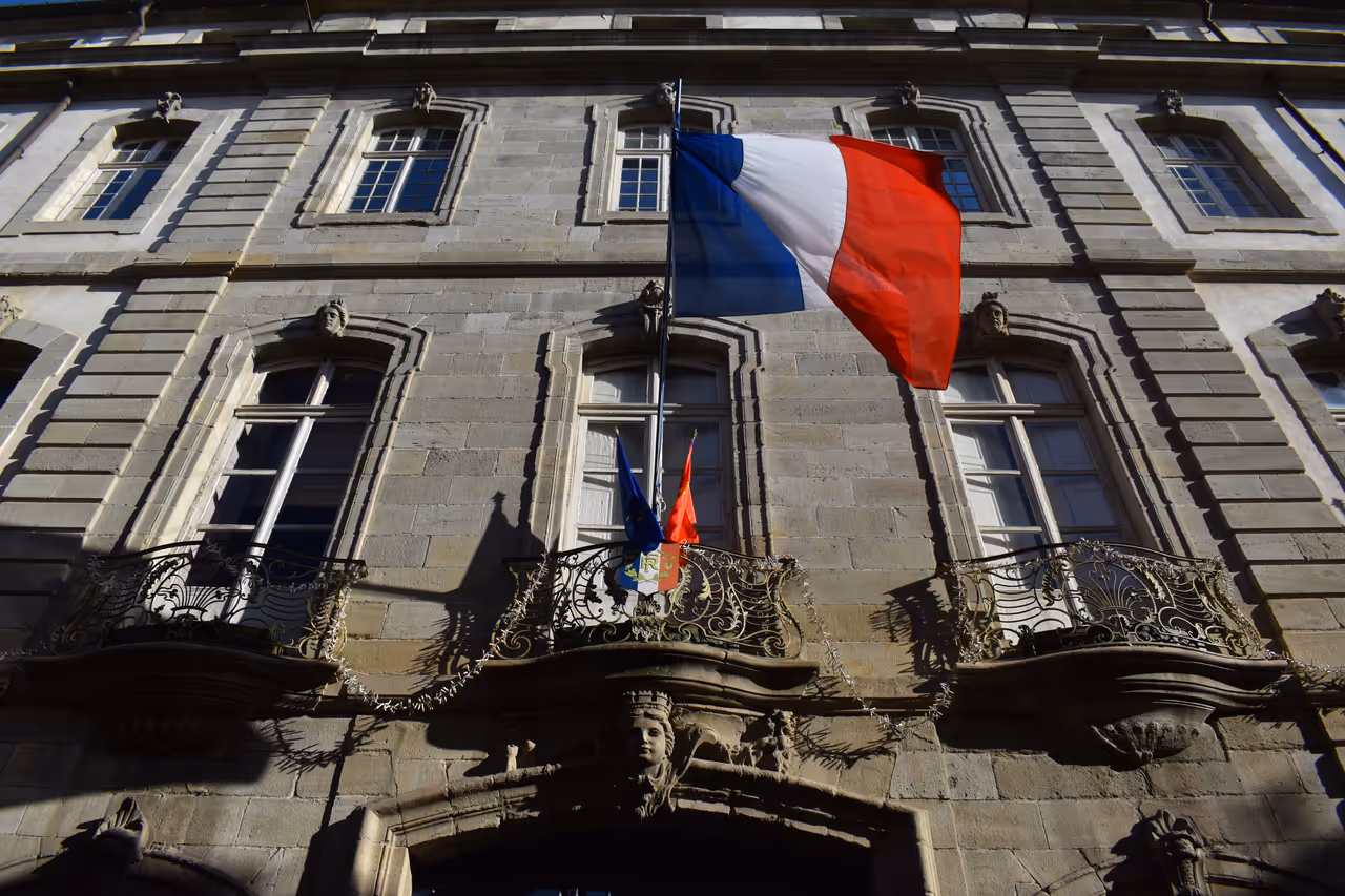 The facade of the Hôtel de Rolland city hall in Carcassonne with a flag flying above ornate balconies