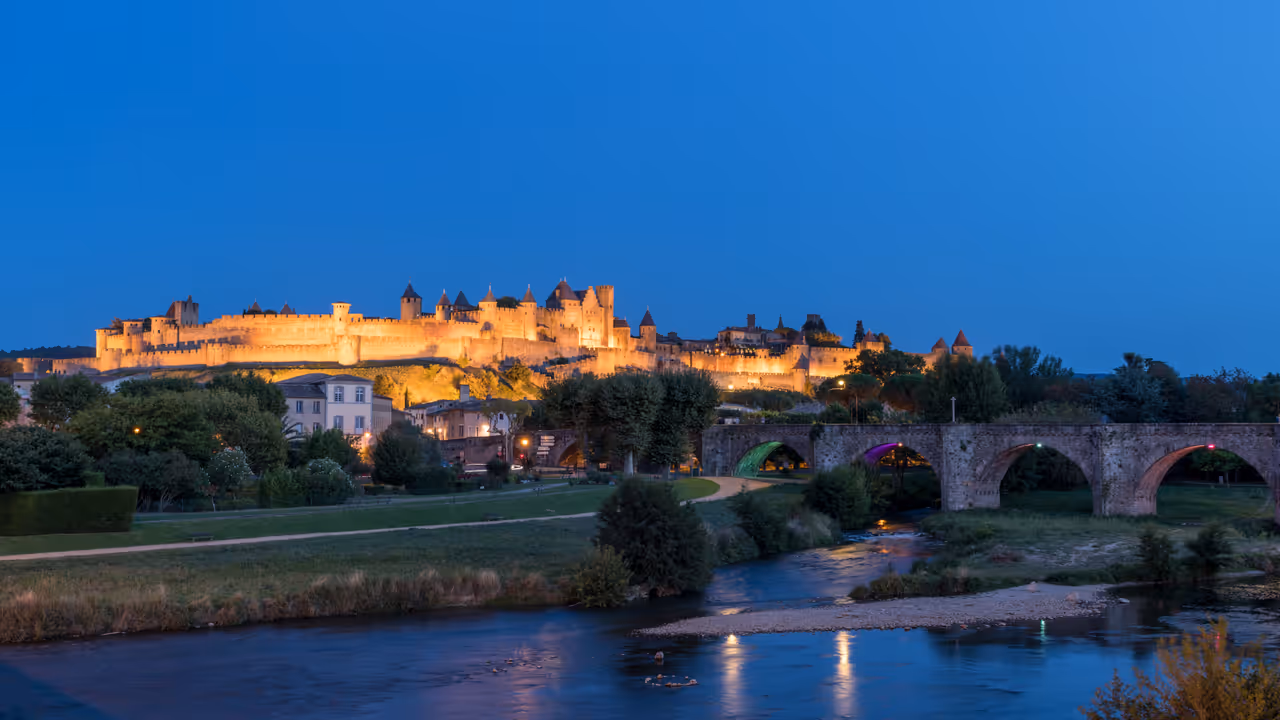 Illuminated medieval fortified city of Carcassonne and stone bridge over the river Aude at dusk