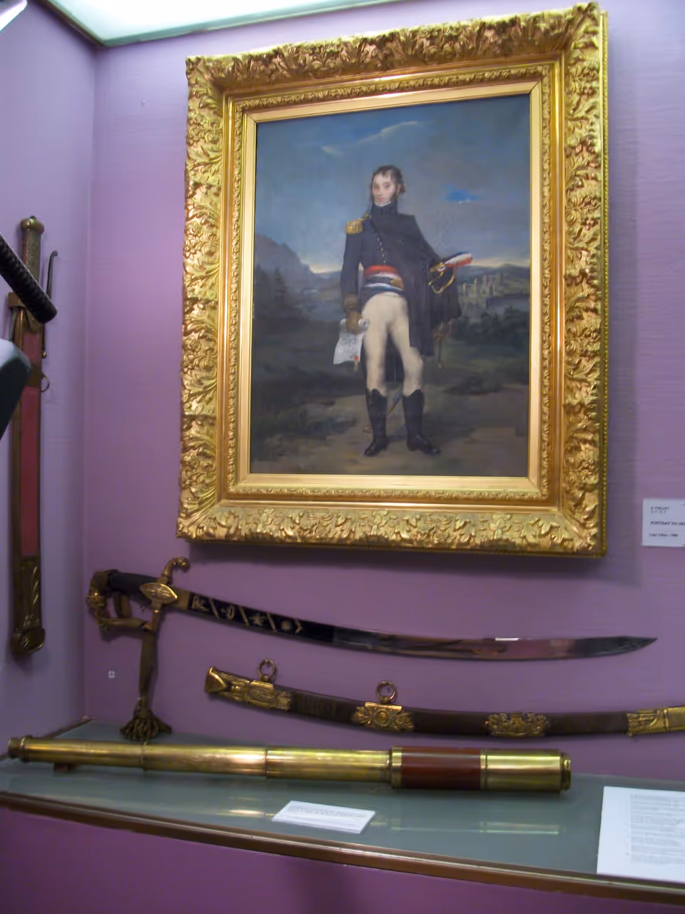 A glass display case containing Napoleon Bonaparte's telescope and swords beneath a framed portrait of him in a museum
