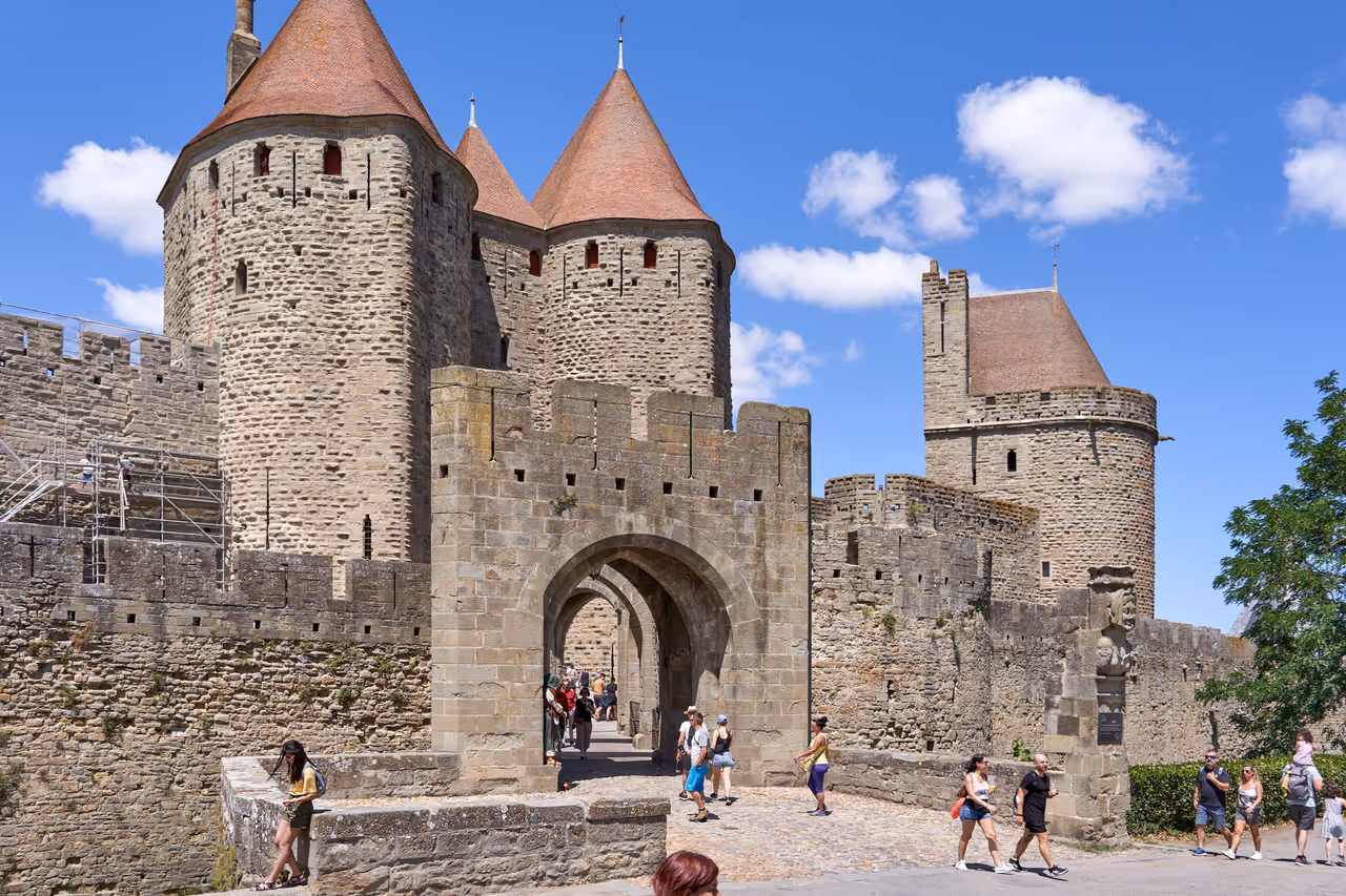 Tourists walking through the historic Porte Narbonnaise stone gateway at the medieval fortified Cité de Carcassonne