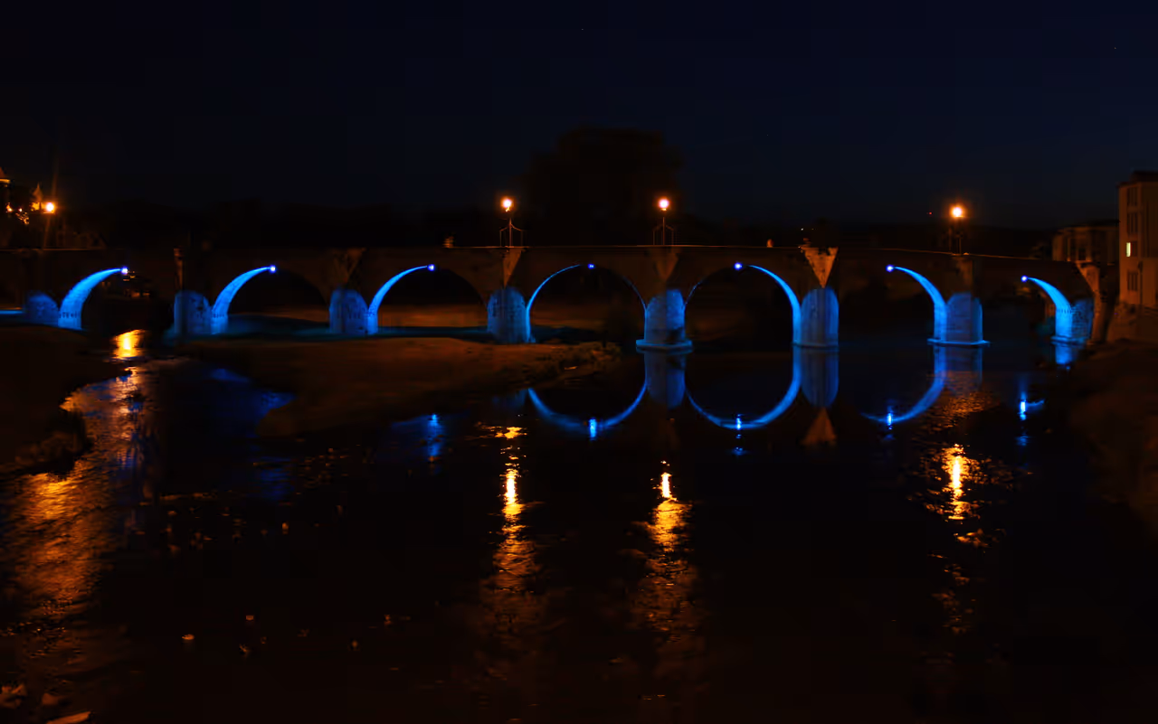 Illuminated mediaeval Pont Vieux bridge arches with blue neon light art installation reflected in the river