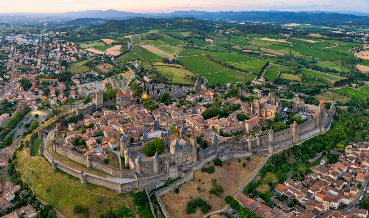 Aerial view of the medieval fortified Cité de Carcassonne surrounded by massive stone walls, watchtowers, and lush green fields