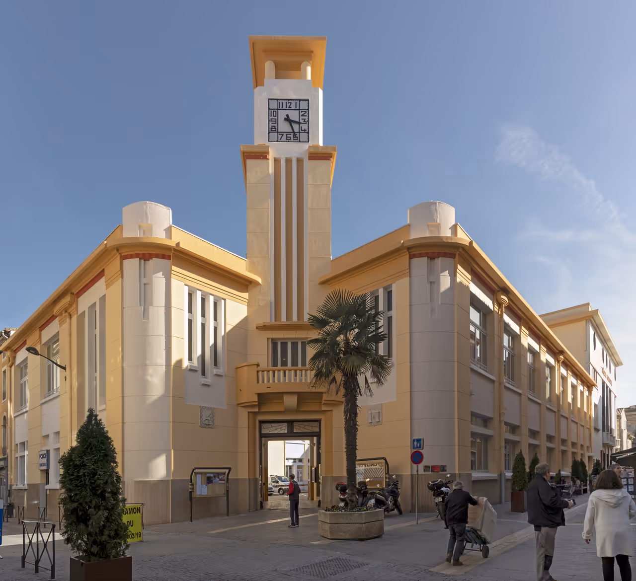 Art Deco municipal police building with a prominent central clock tower under a clear blue sky in Carcassonne