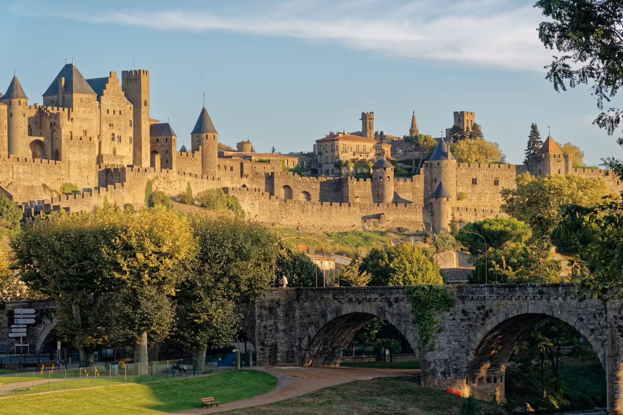 Panoramic view of the medieval fortified Cité de Carcassonne, showcasing its stone walls, watchtowers, and the historic Pont Vieux arch bridge under a clear sky