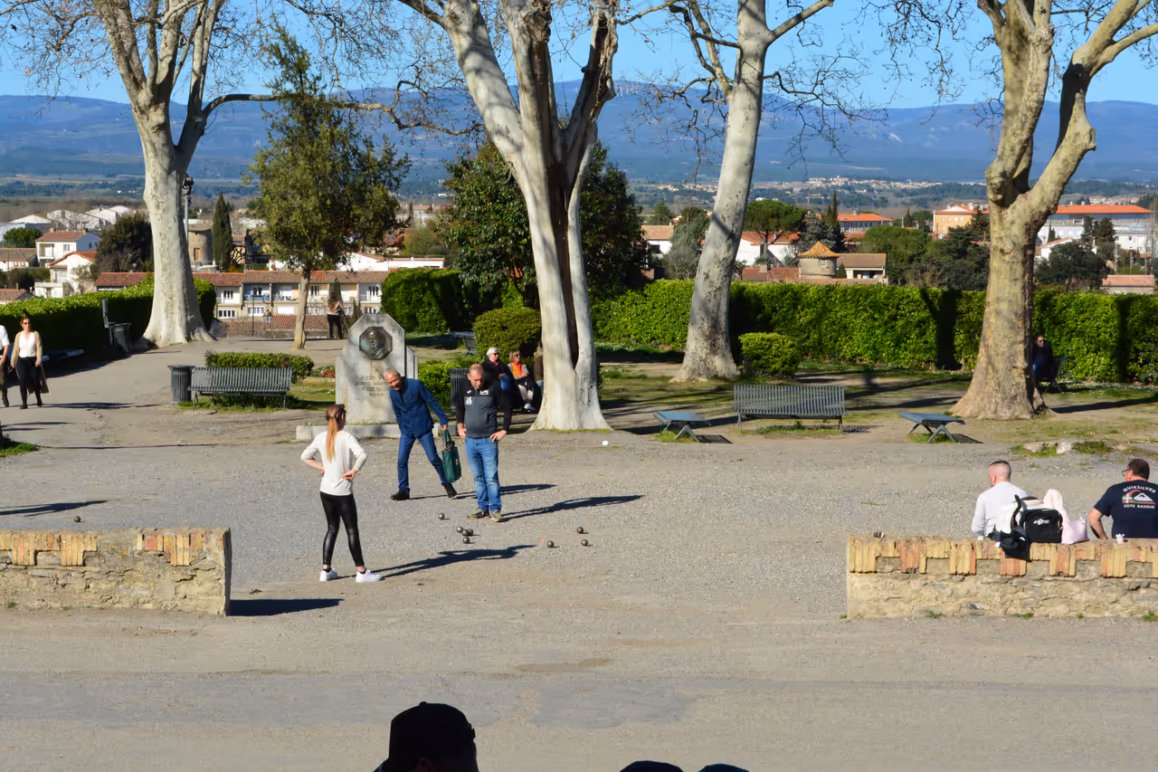 People playing boules in a sunlit plaza outside Porte Narbonnaise in Carcassonne