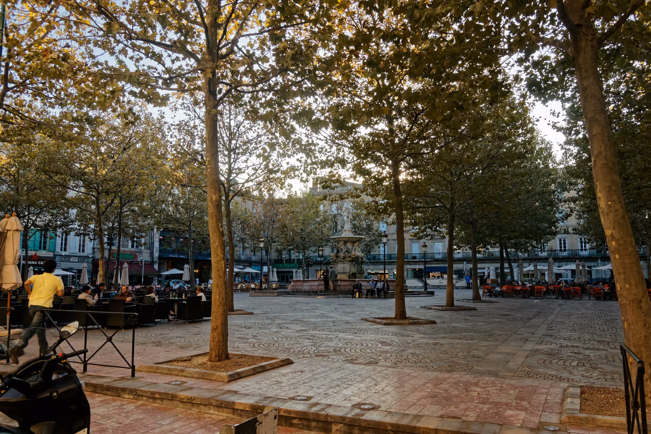 Shaded outdoor cafe seating and historic fountain at Place Carnot in Carcassonne
