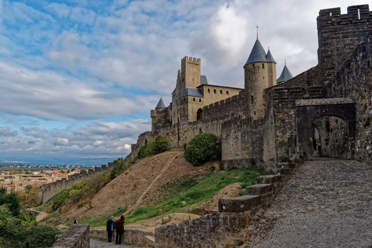 Stone pathway leading to the Porte d'Aude gateway at the medieval fortified Cité de Carcassonne with stone walls and towers under a cloudy sky
