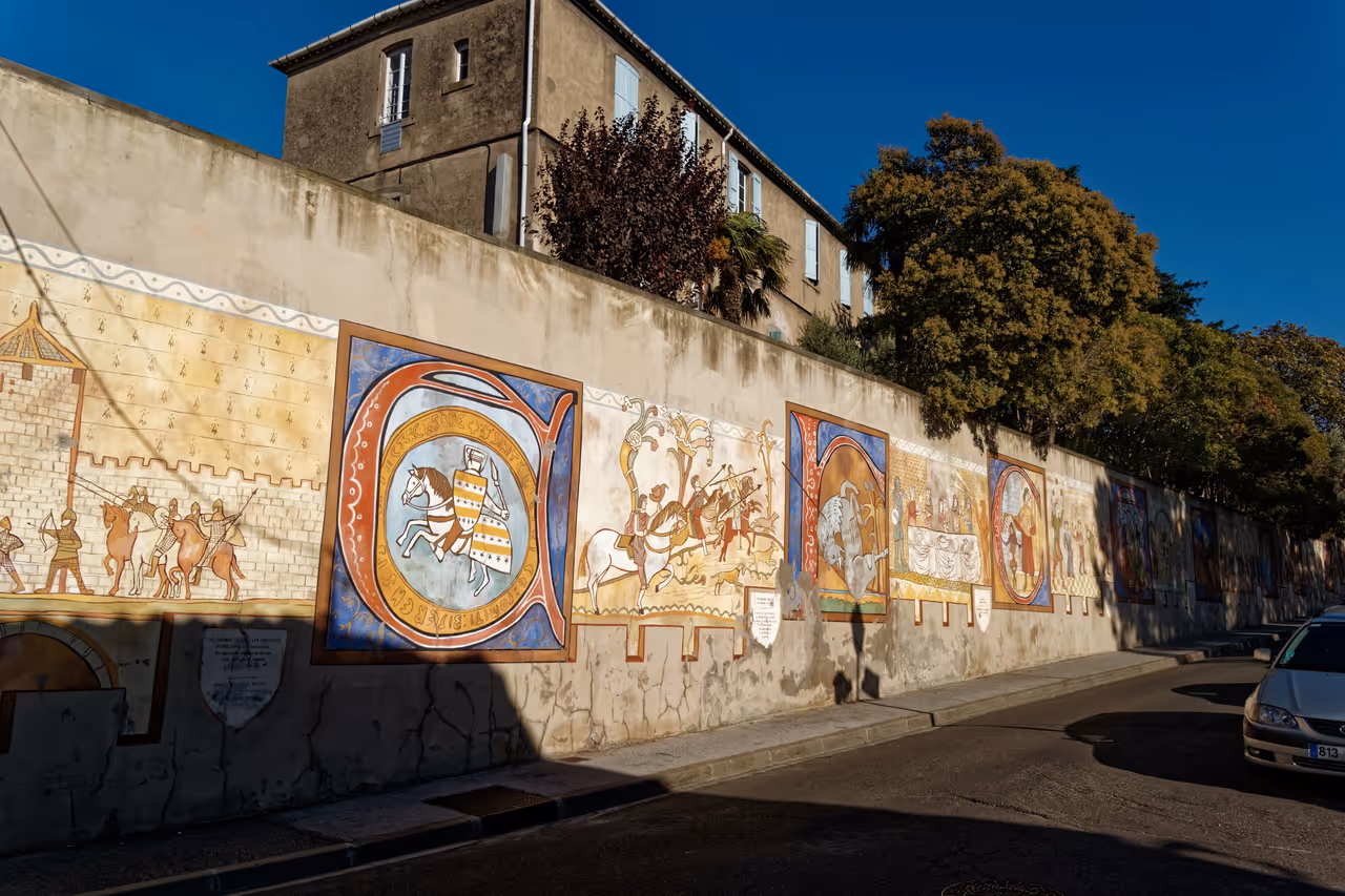 Large medieval-style mural painted on a stone retaining wall along Rue Trivalle in Carcassonne