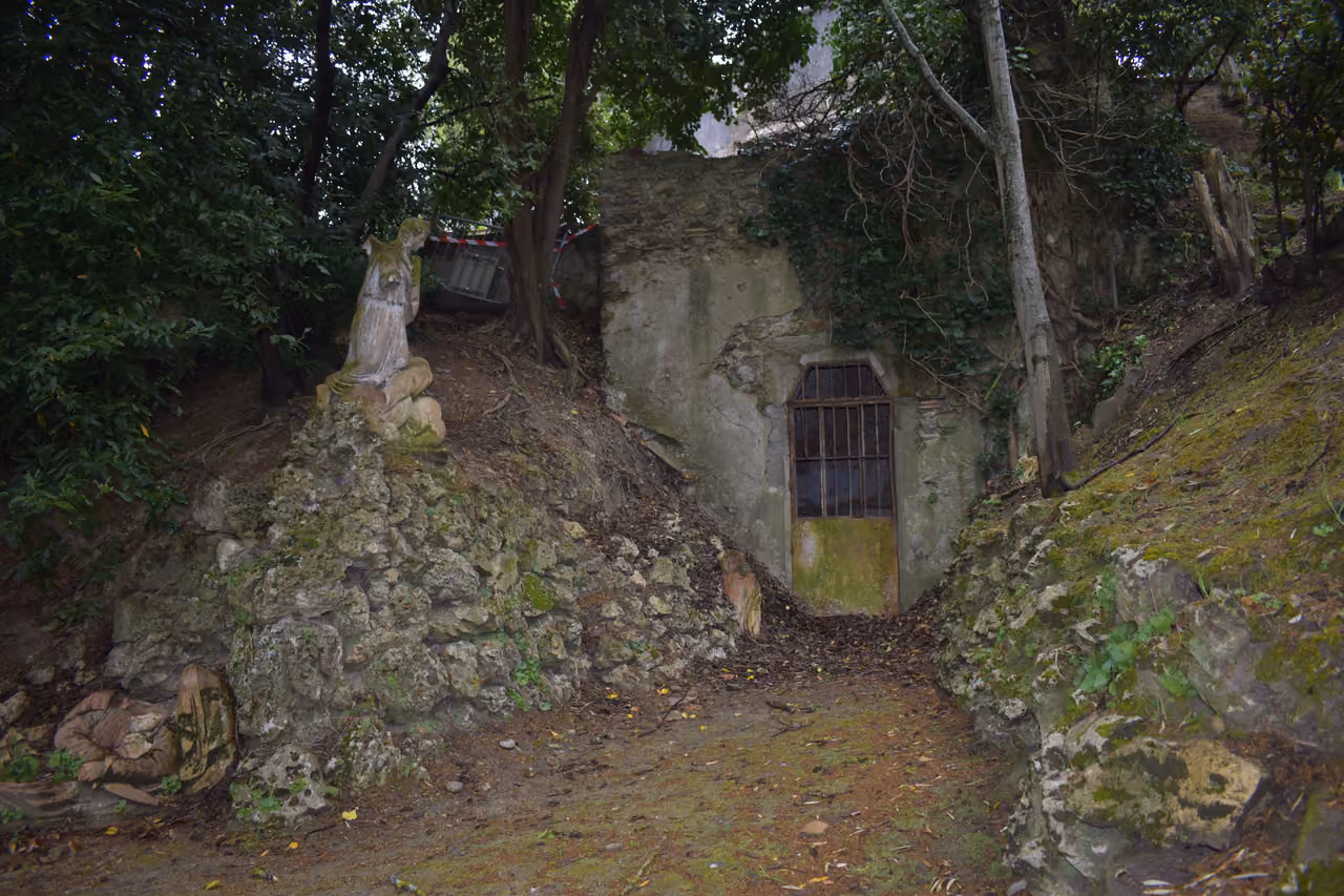Stone tomb entrance and religious statue surrounded by trees in the Jardin du Calvaire, Carcassonne