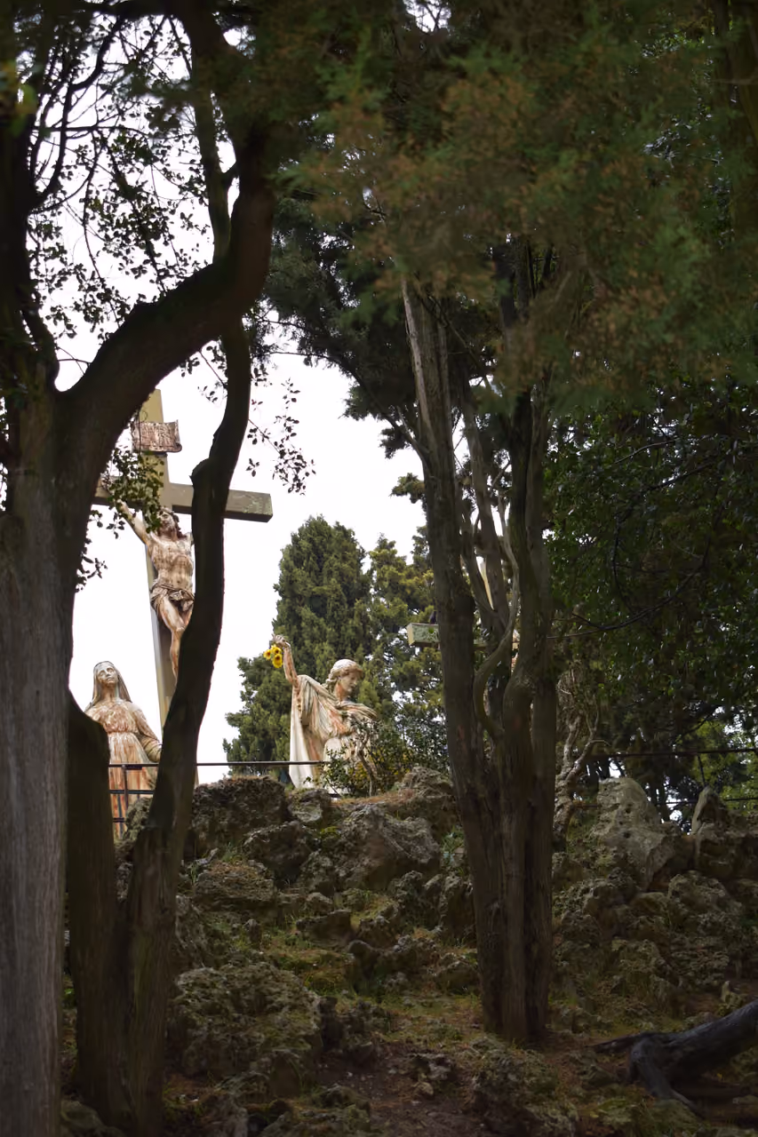 Religious statues and a large crucifix framed by trees in the Jardin du Calvaire in Carcassonne