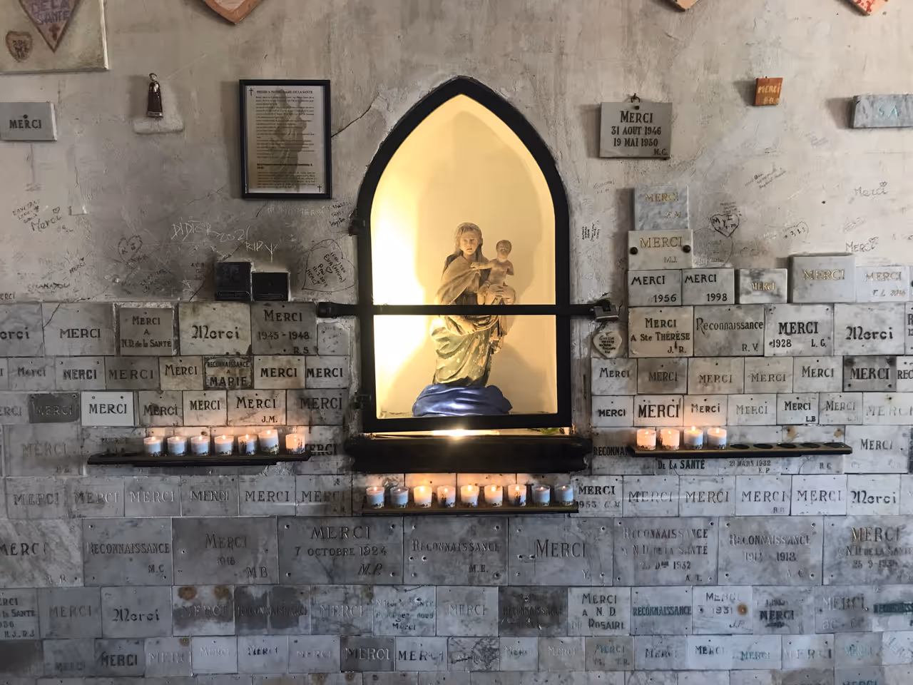 Interior of Chapelle Notre-Dame-de-Santé in Carcassonne showing a statue of the Virgin Mary and Child surrounded by ex-voto thanksgiving plaques and candles