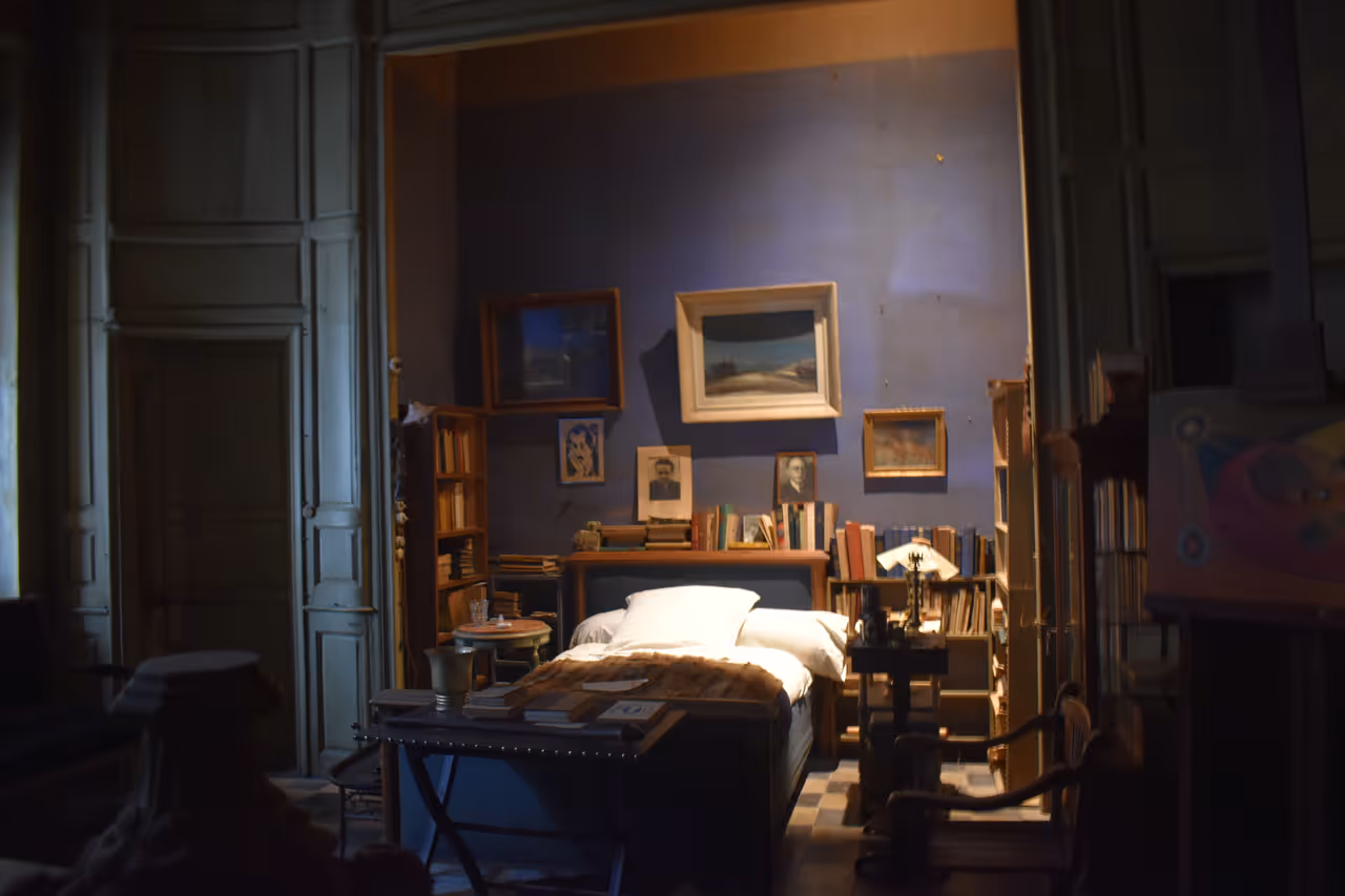 Preserved bedroom of poet Joë Bousquet inside the Maison des Mémoires museum in Carcassonne with blue walls, a central bed, bookshelves and historic paintings