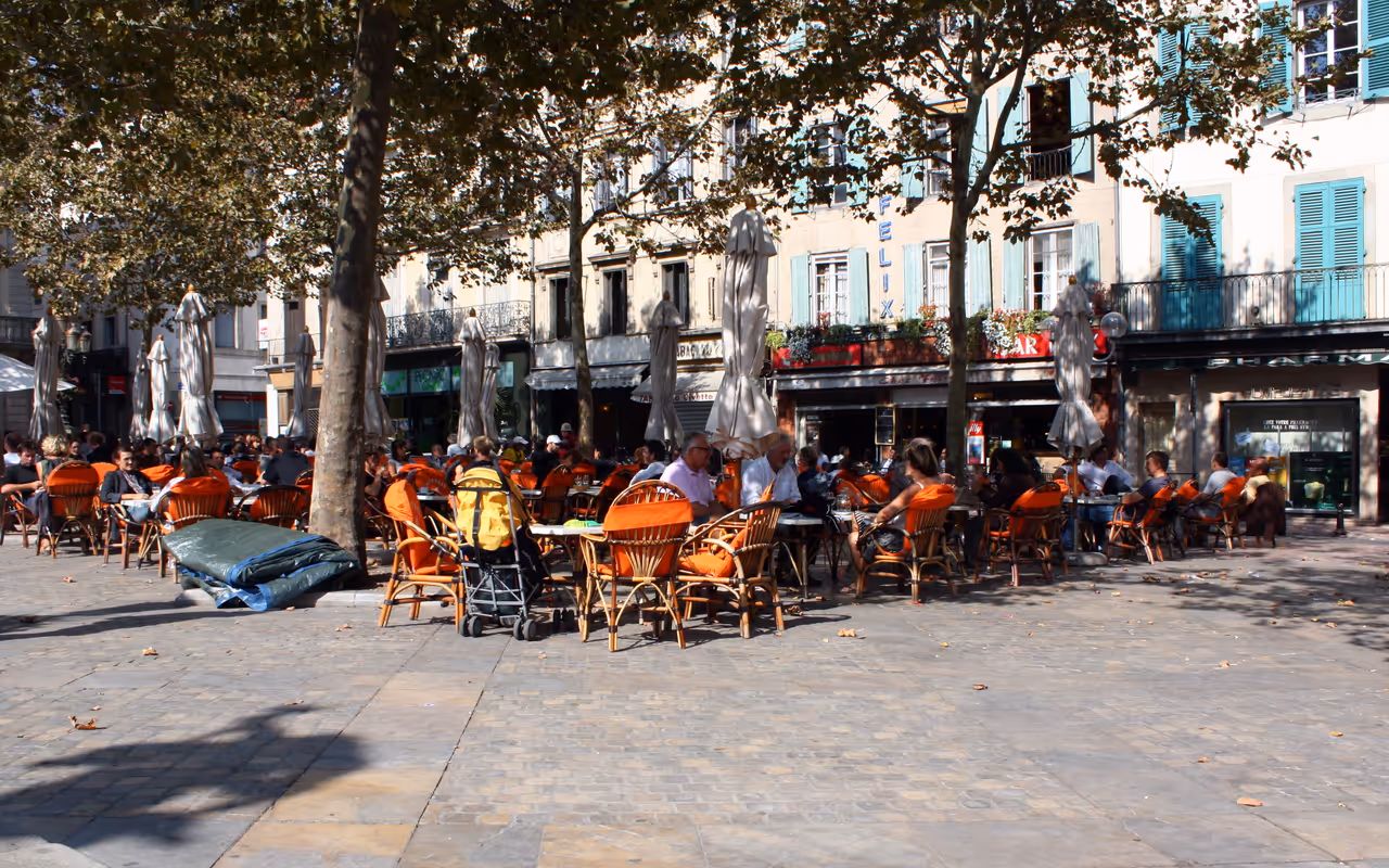 Outdoor cafe with orange chairs on a sunlit plaza lined with trees in Carcassonne