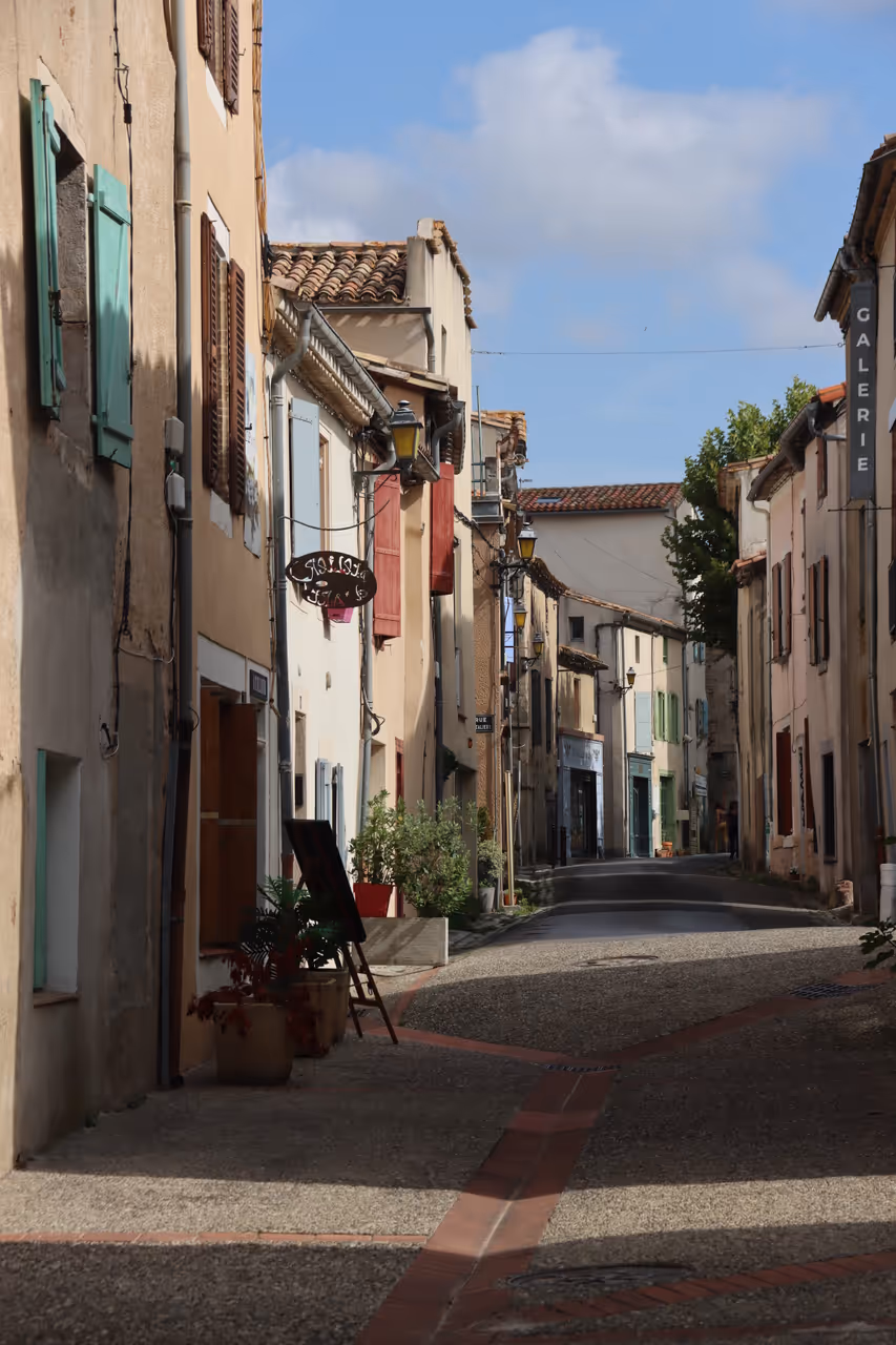 Narrow cobblestone street in Montolieu lined with historic houses and colorful shutters
