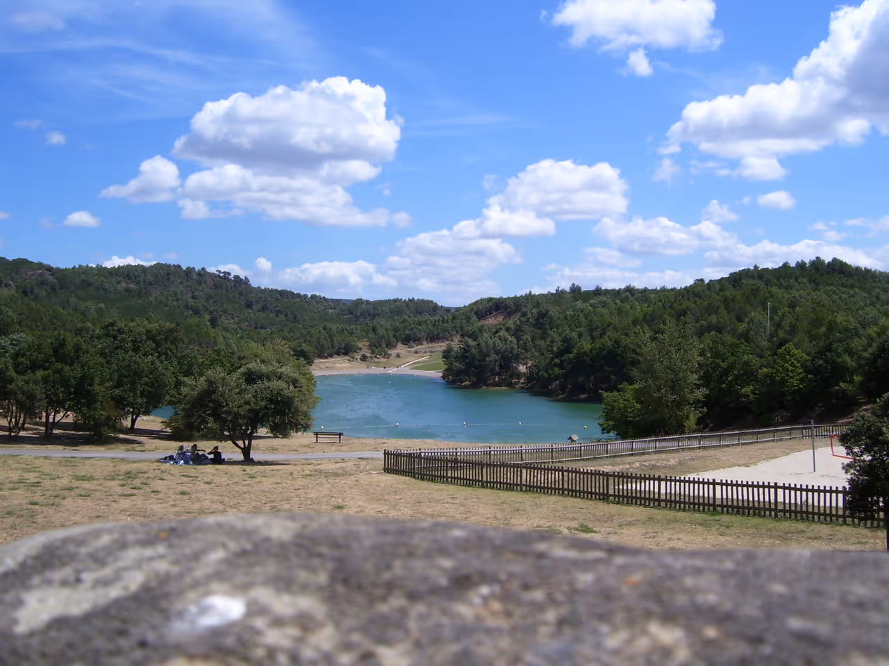 Scenic view of the sandy beach and clear blue waters at Lac de la Cavayère near Carcassonne surrounded by lush green pine forests under a sunny sky