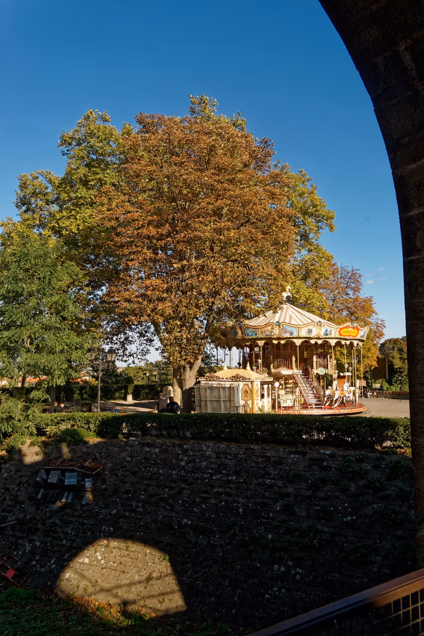 View east from the Carcassonne citadel drawbridge toward a vintage merry-go-round carousel and autumn trees