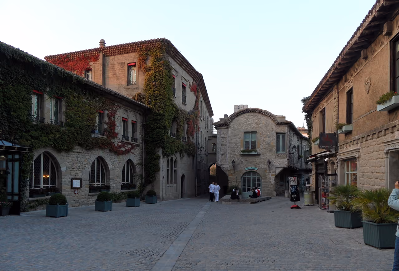 Cobblestone square surrounded by historic stone buildings covered in ivy with a narrow street in a medieval European town