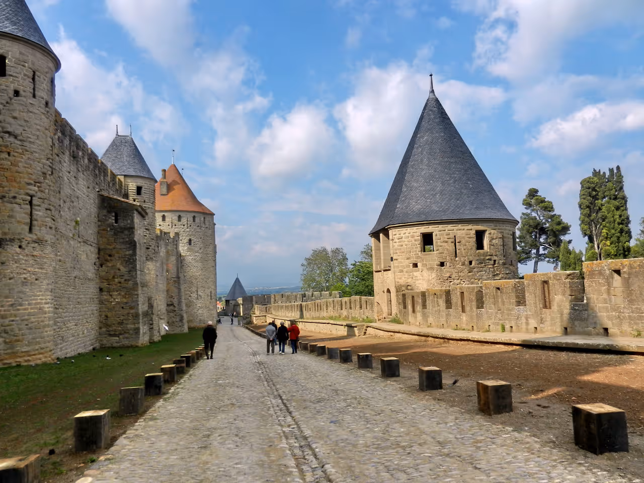 Cobblestone walkway between the medieval stone walls and conical-roofed towers of the fortified Cité de Carcassonne