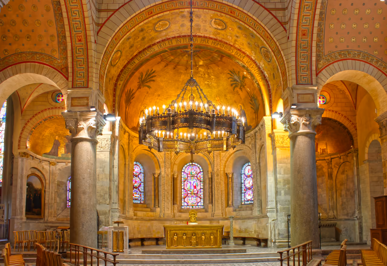 Interior of the Romanesque Basilica of Saint Martin d'Ainay featuring a large corona lucis chandelier, stained glass windows, and painted arches