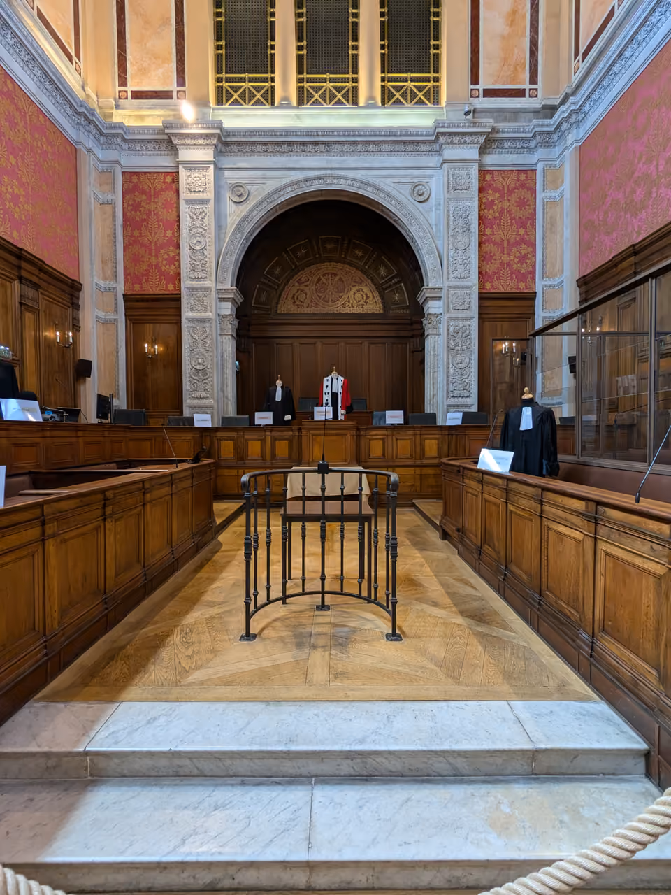 Historic courtroom interior inside Palais de Justice featuring Salle des Assises with ornate wood-panelled seating, stone arches and decorative pink walls
