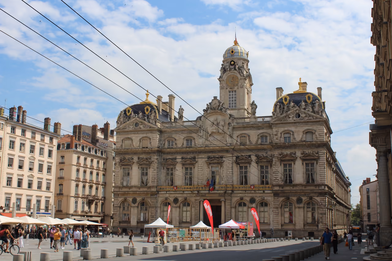 The majestic facade of the Hôtel de Ville at Place des Terreaux under a cloudy blue sky