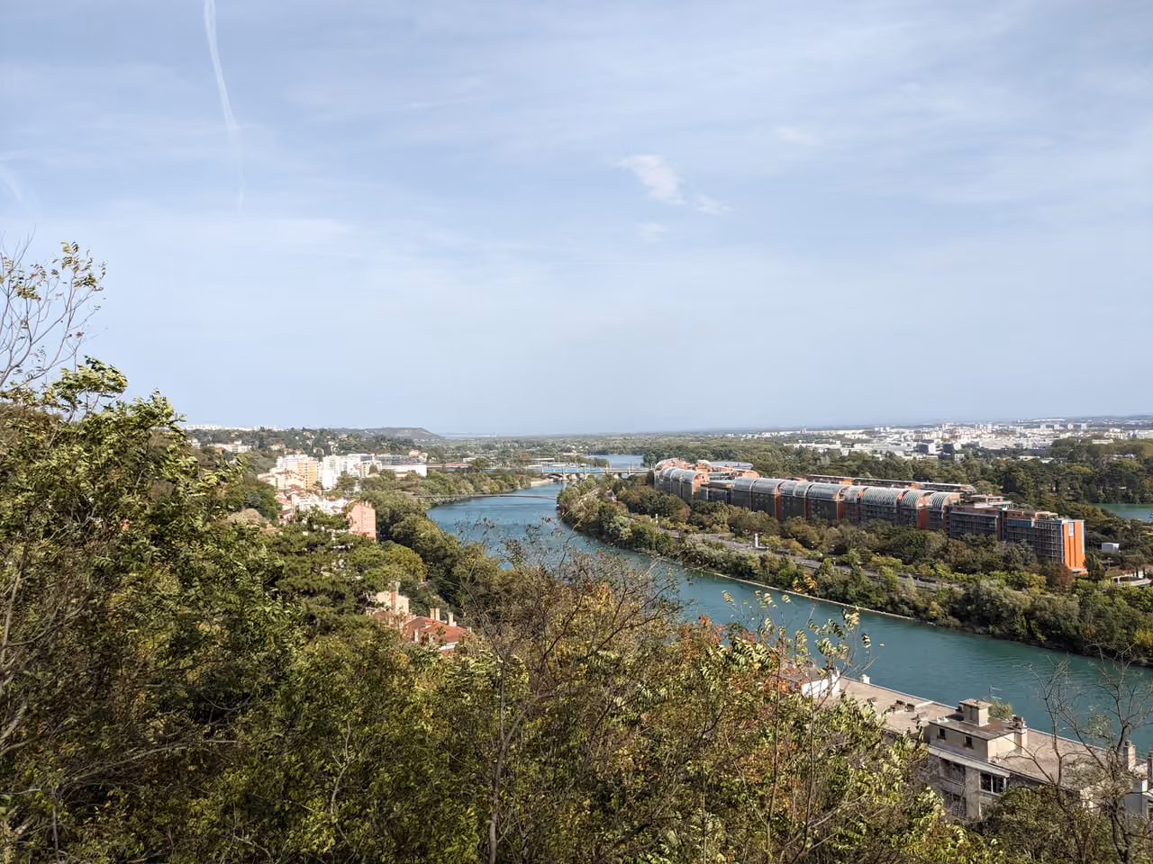 Panoramic view of a river winding through trees towards a modern city under a clear sky