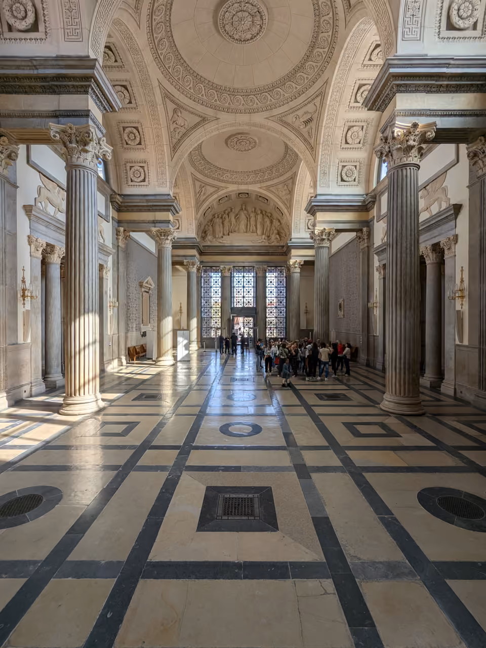 Wide view of the grand Salle des Pas Perdus hall inside the historic Palais de Justice in Lyon showing high vaulted ceilings, classical columns and patterned tiled floors
