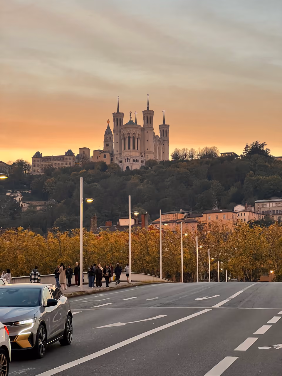 View from a bridge looking up at the illuminated Basilica of Notre-Dame de Fourviere on a hill during a golden sunset