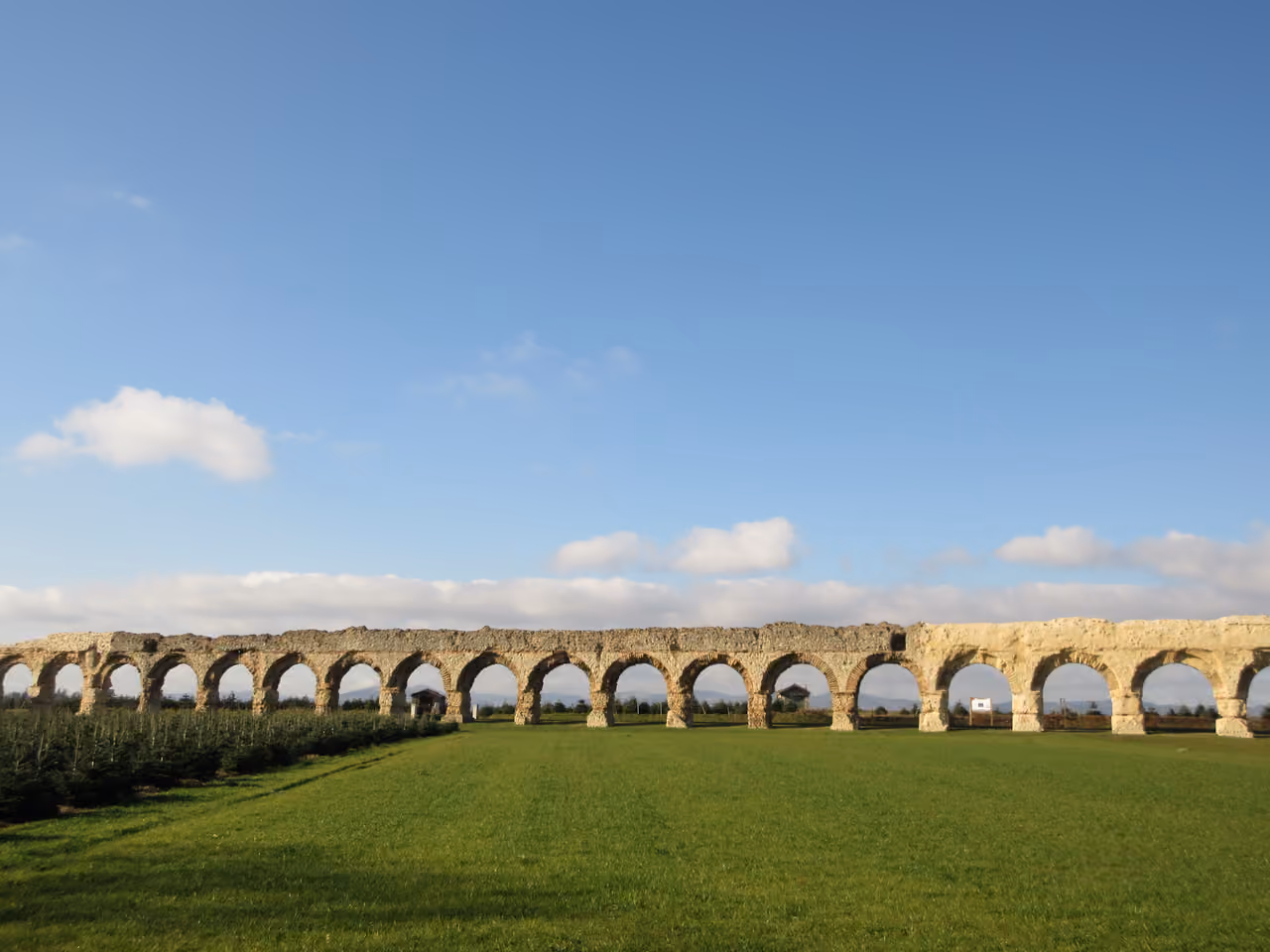 Ancient stone Roman aqueduct standing in a green grassy field under a blue sky