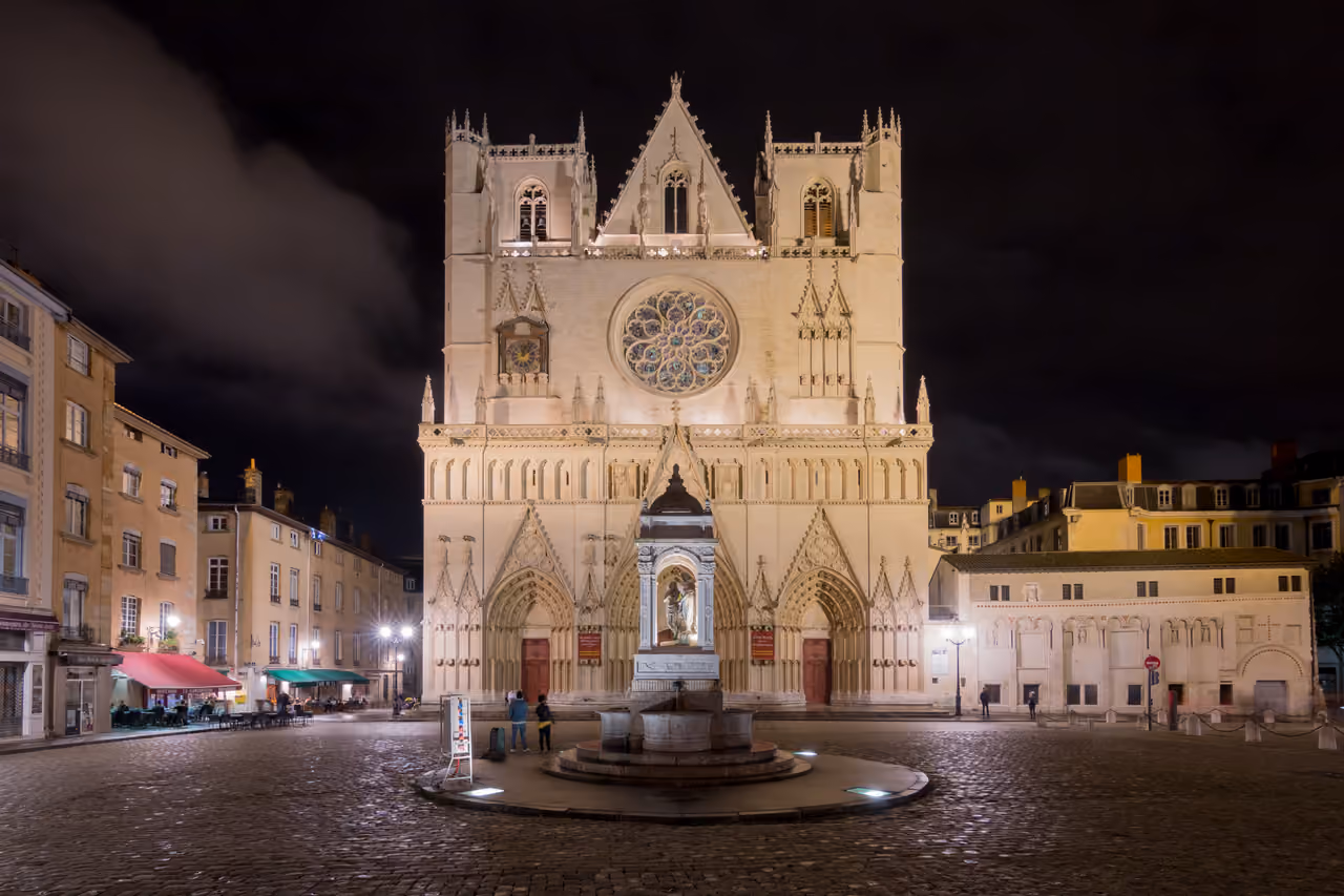 The illuminated facade of Saint-Jean-Baptiste Cathedral at night in the cobblestone square of Place Saint-Jean