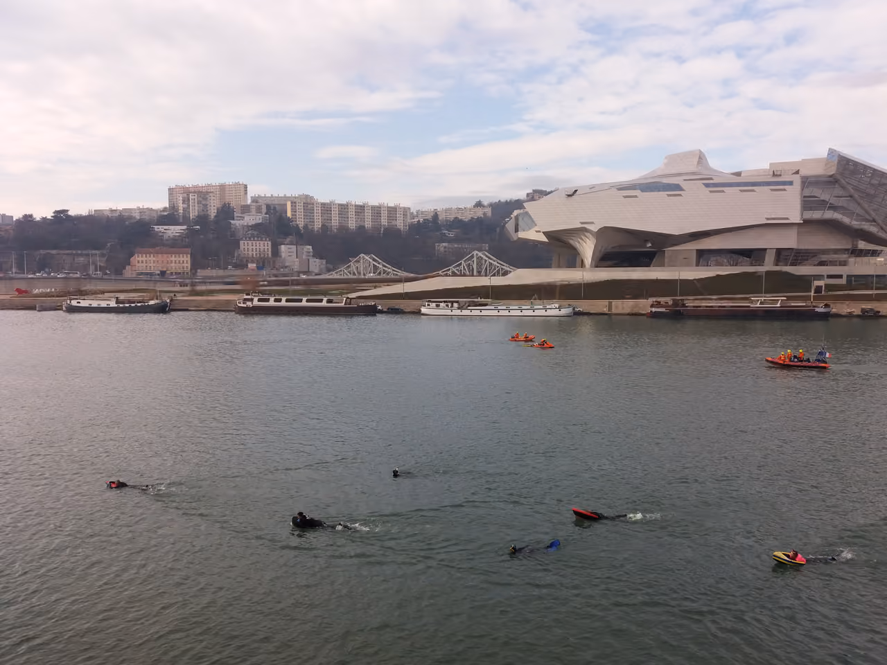 Swimmers participating in the Traversée de Lyon swimming event on the Rhône River near the Musée des Confluences
