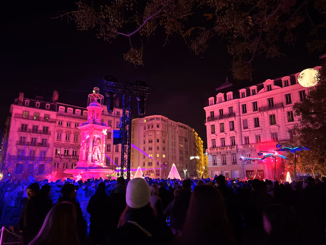 Crowd gathered at Place des Jacobins fountain illuminated with pink lights during the Fête des Lumières