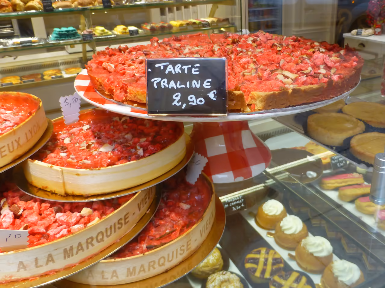A traditional pink pralines tart on display at a French bakery with a handwritten price sign