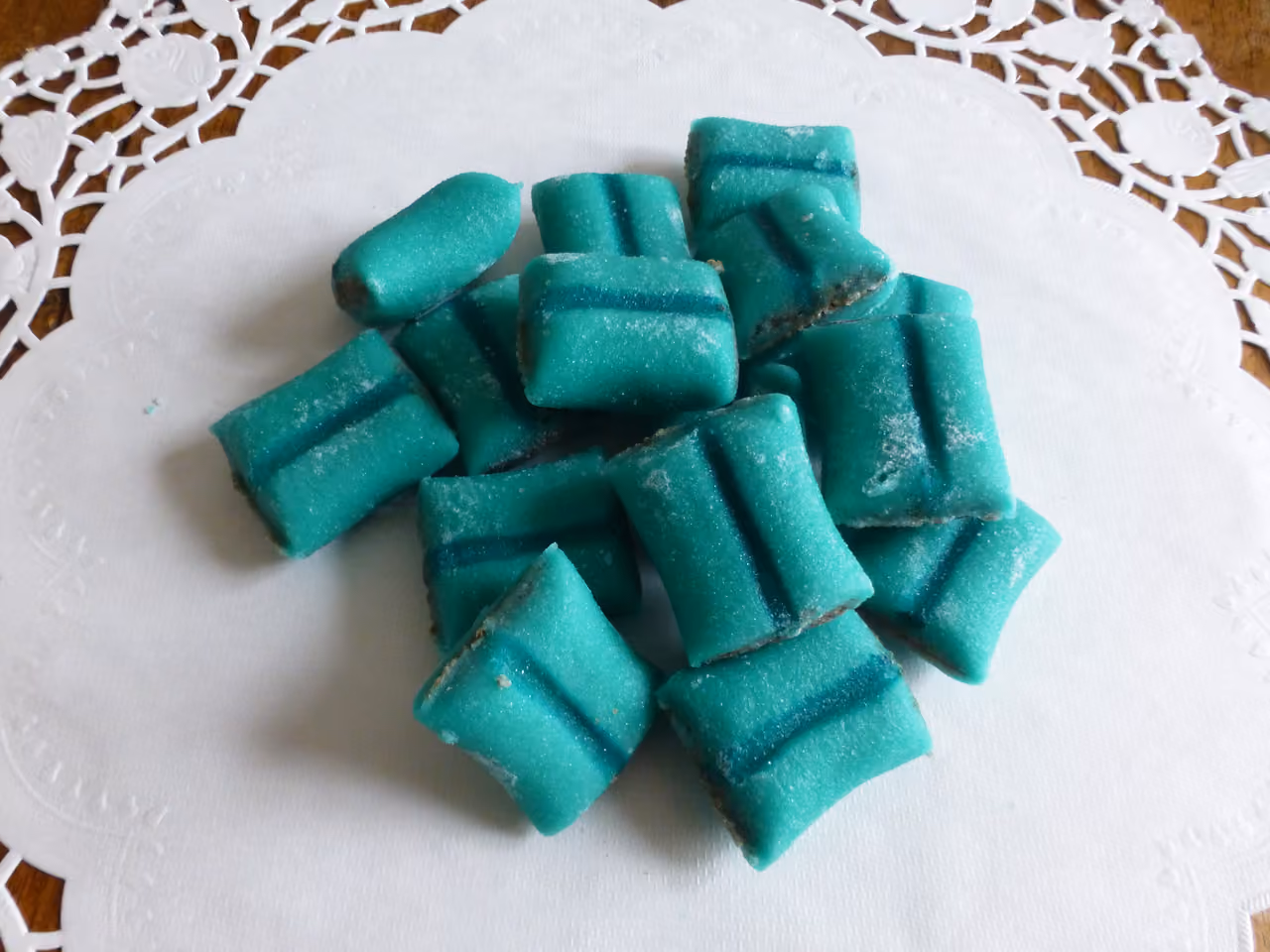 Traditional turquoise marzipan cushion sweets on a white lace paper doily