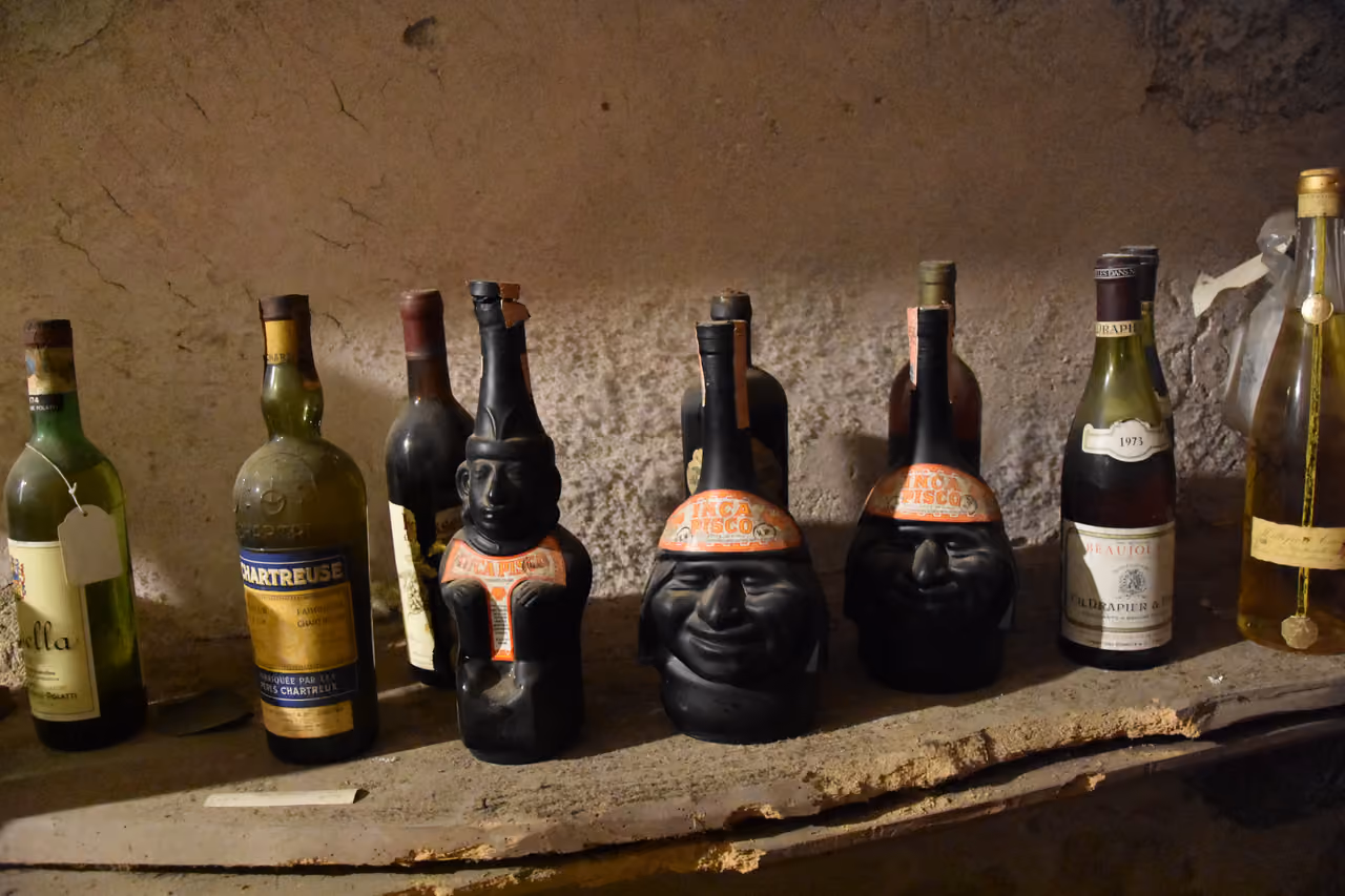 Vintage wine and liqueur bottles on a rustic wooden shelf inside Villa Della Porta Bozzolo