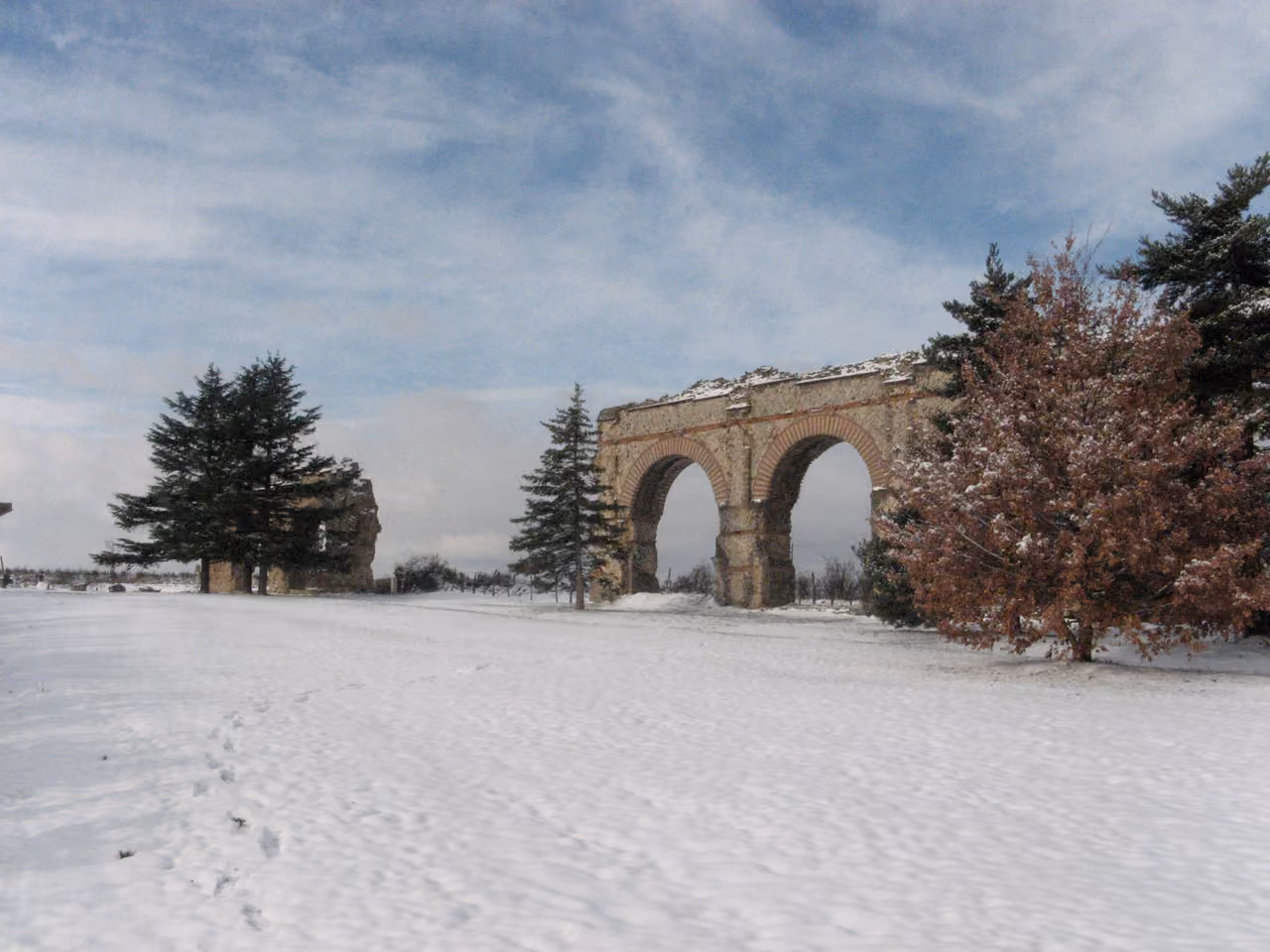 Ancient Roman arches of the Gier Aqueduct standing in a snow-covered field under a cloudy sky