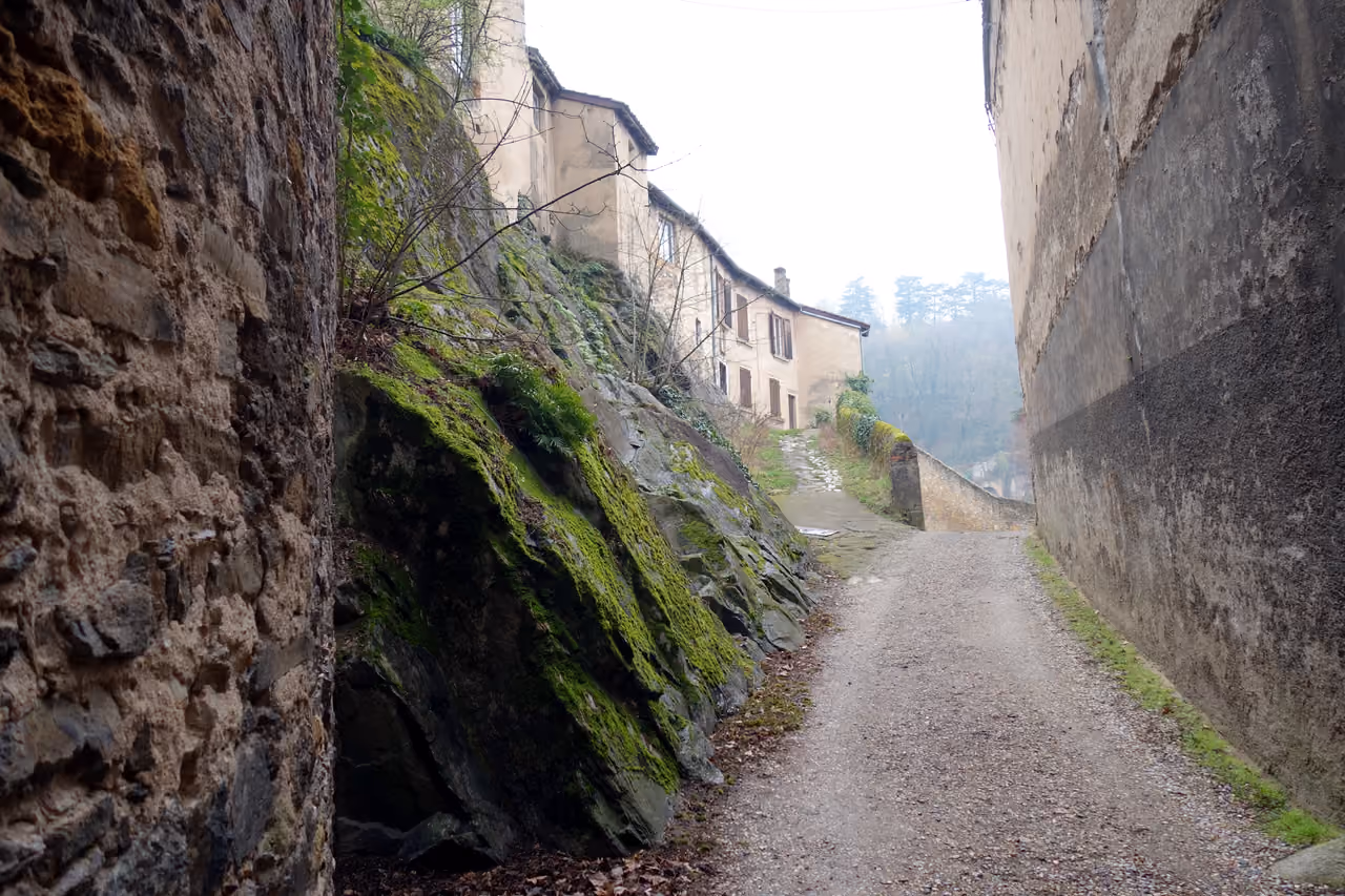 Narrow gravel path between historic stone walls leading to old village houses on Île Barbe