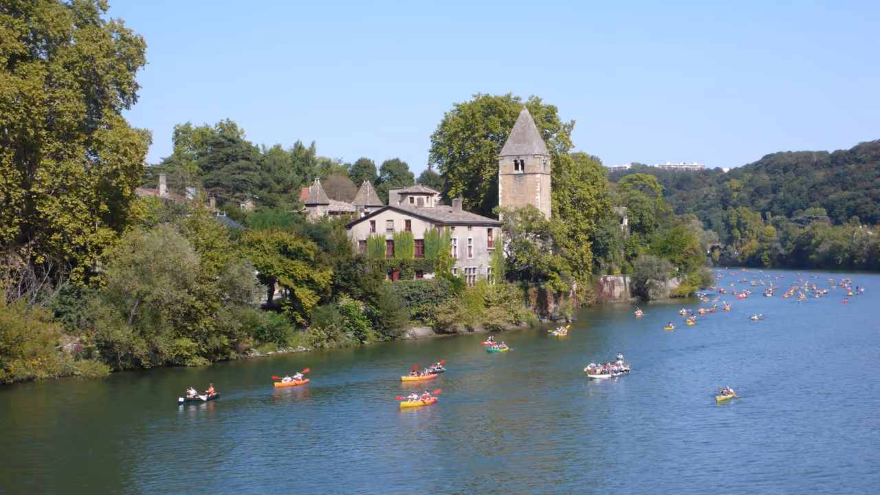 Kayaking regatta on the Saone River passing by the medieval Church of Notre-Dame on l'Ile Barbe