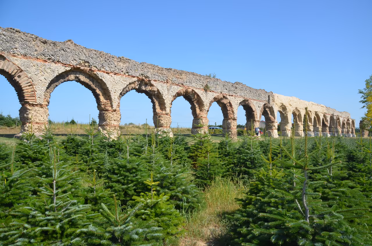 An ancient Roman stone archway structure of the Aqueduct of the Gier stretching across a green field under a clear blue sky