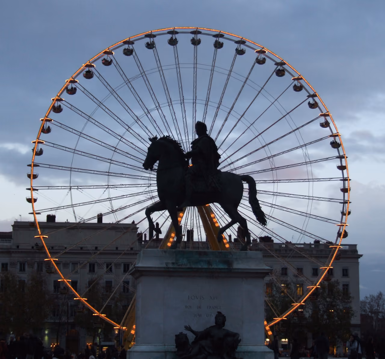 Silhouette of the equestrian statue of Louis XIV framed perfectly by a glowing Ferris wheel at dusk in Place Bellecour