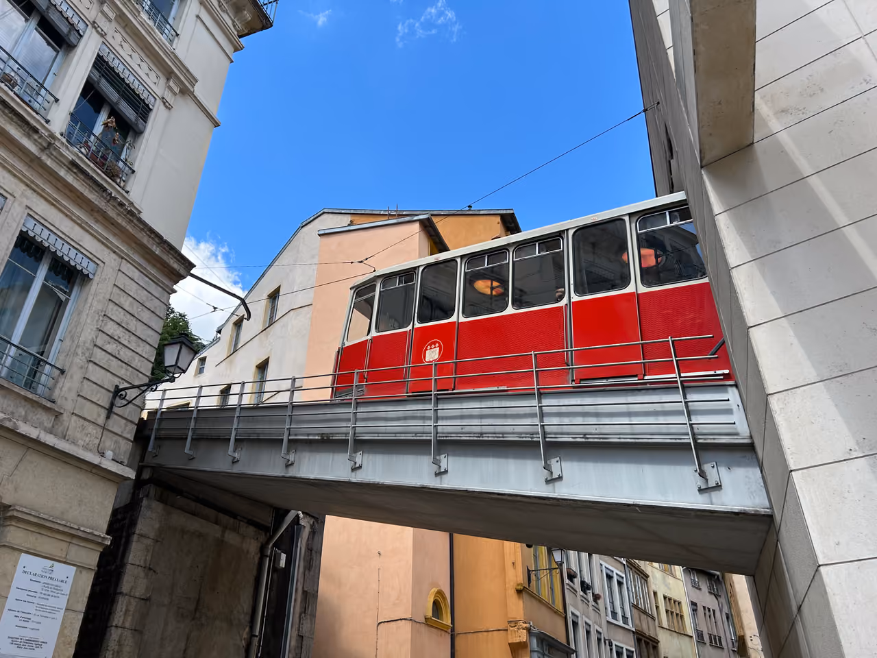 Red and white Fourvière funicular railway carriage crossing a bridge above Rue Tramassac