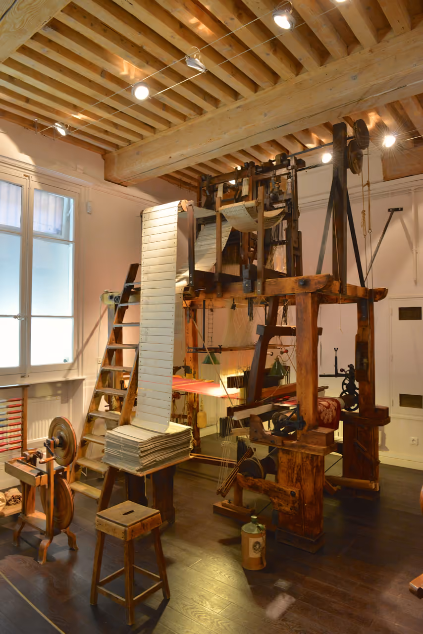A historic Jacquard loom with punch cards displayed inside the Maison des Canuts museum