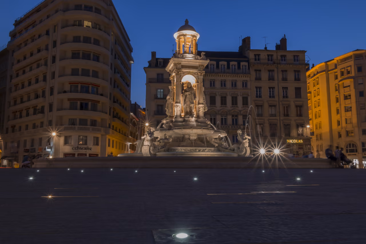 Lit monument at Place des Jacobins at night with fountain lit up