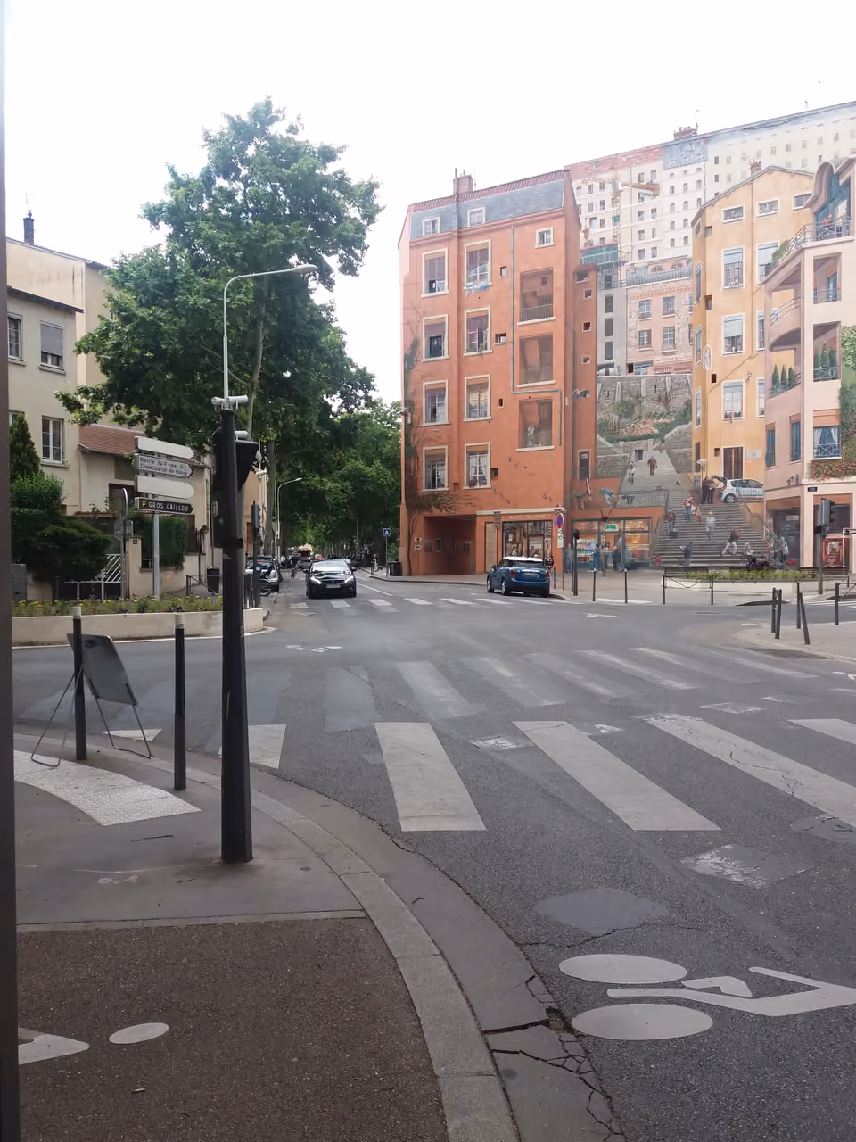 Street view of the Mur des Canuts trompe-l’oeil mural viewed from across a pedestrian crossing
