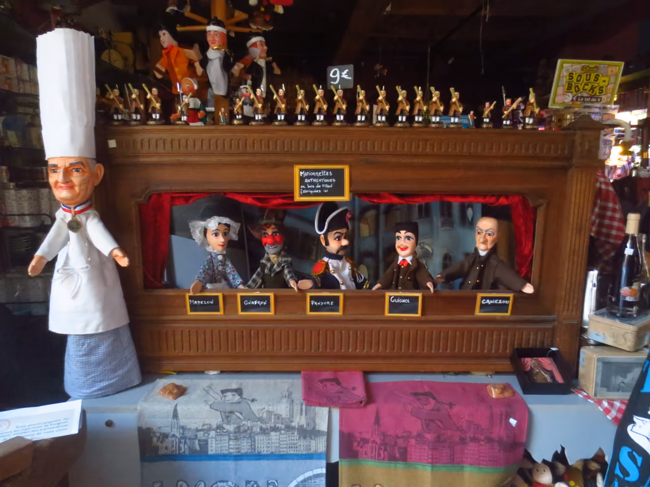 Traditional Guignol puppet theatre display featuring a large Paul Bocuse chef puppet and a row of smaller marionettes on a wooden stage in a boutique shop