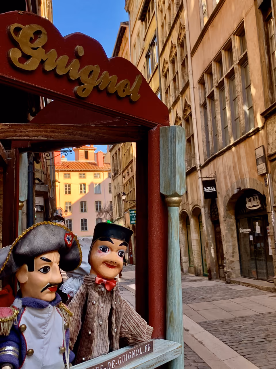 Two traditional Guignol puppets in a miniature theatre on a cobbled street in Vieux Lyon