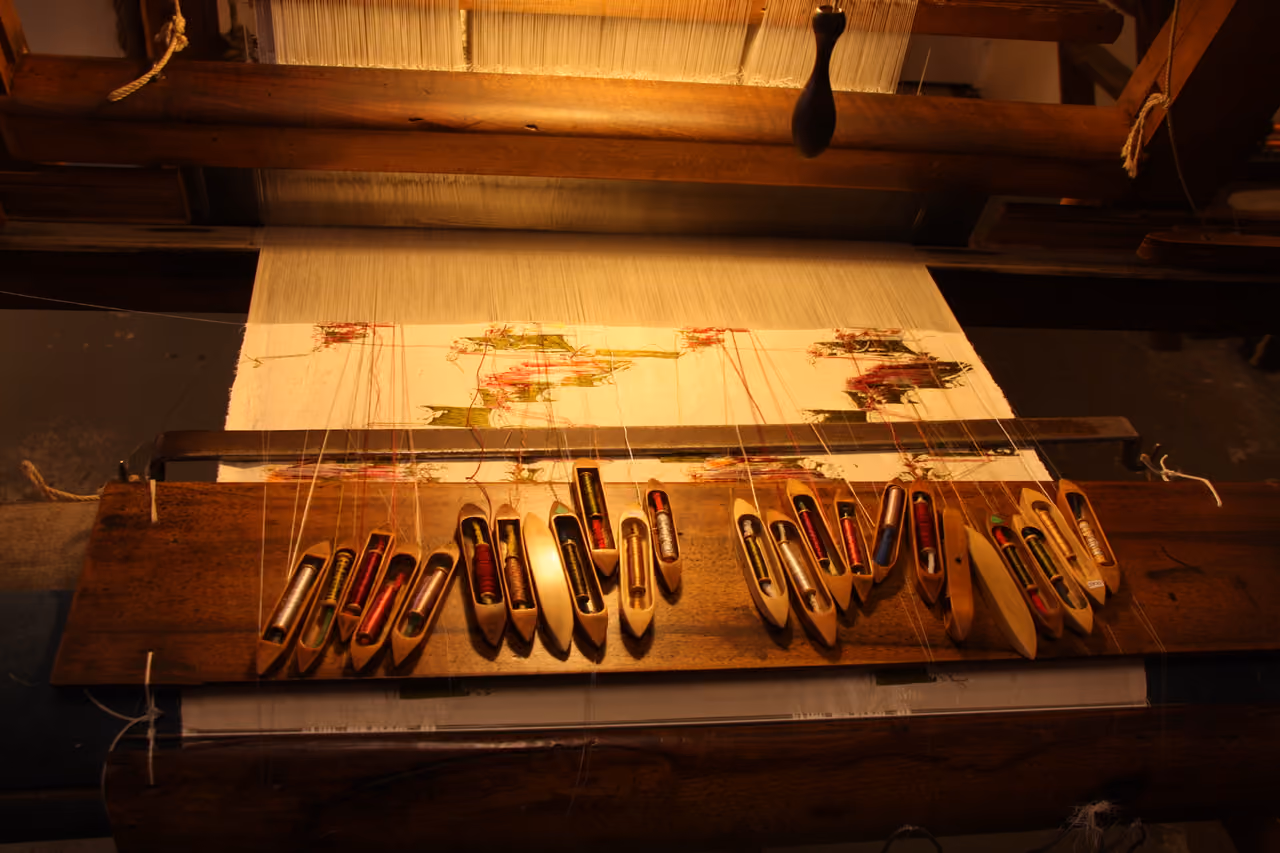 A traditional Jacquard silk loom with multiple wooden weaving shuttles and colorful threads at the Maison des Canuts museum
